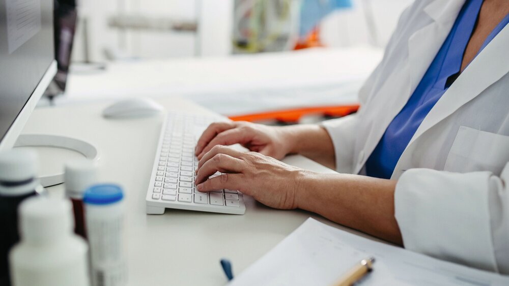 Nahaufnahme eines Arztes bei der Arbeit am Computer in einer Arztpraxis. Arzt macht Papierkram und Verwaltung.