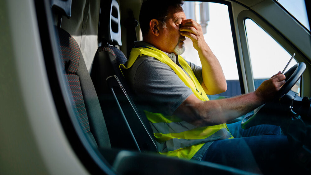 Ein älterer Mann, der sich die Augen reibt, sitzt am Steuer eines Transporters. Ein älterer Mann, der sich die Augen reibt, sitzt am Steuer eines Transporters.