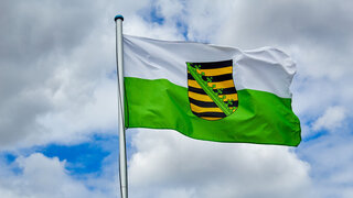 Die sächsische Flagge weht vor einem blauen Himmel mit Wolken