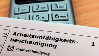 Eine Arbeitsunfähigkeitsbescheinigung liegt auf einem Telefon
