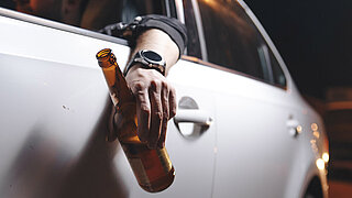 Ein betrunkener junger Mann fährt mit einer Flasche Bier im Auto.