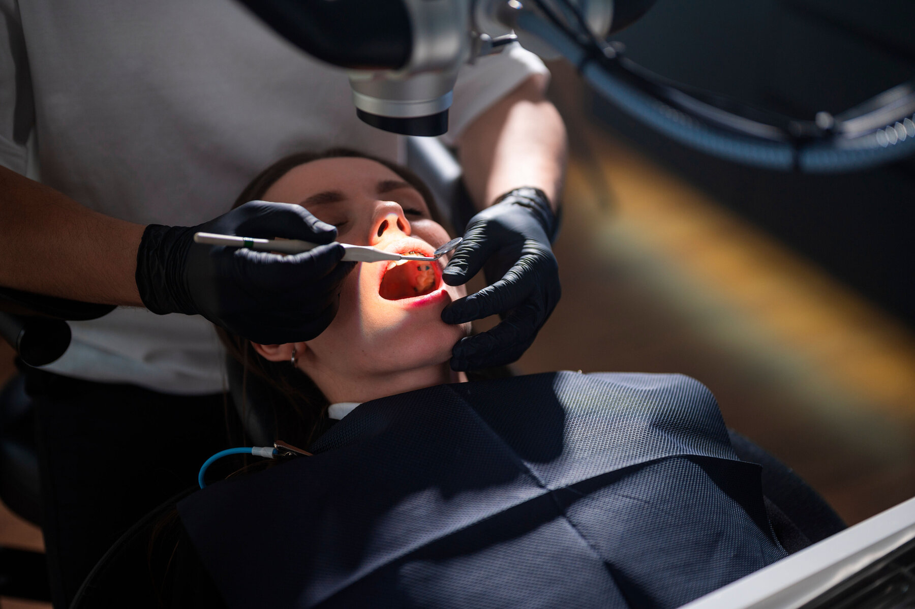 Restorative Dentist Operating On Patient Mouth Using Microscope And Rotary Instruments, Gloved Hands