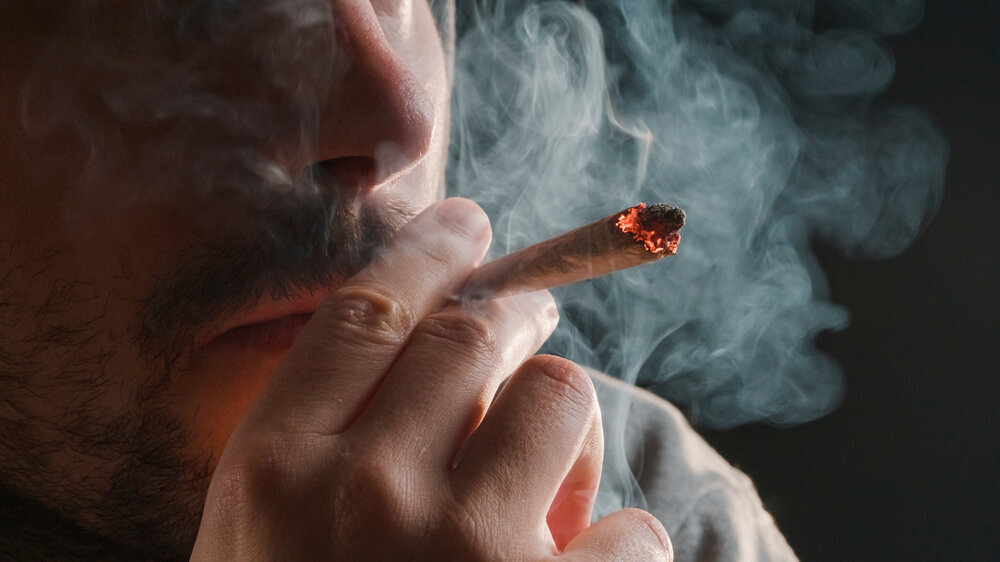 Man smoking a marijuana weed joint, inhaling cannabis smoke.
