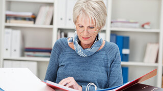 Altere Mitarbeiterin blättert in Unterlagen.