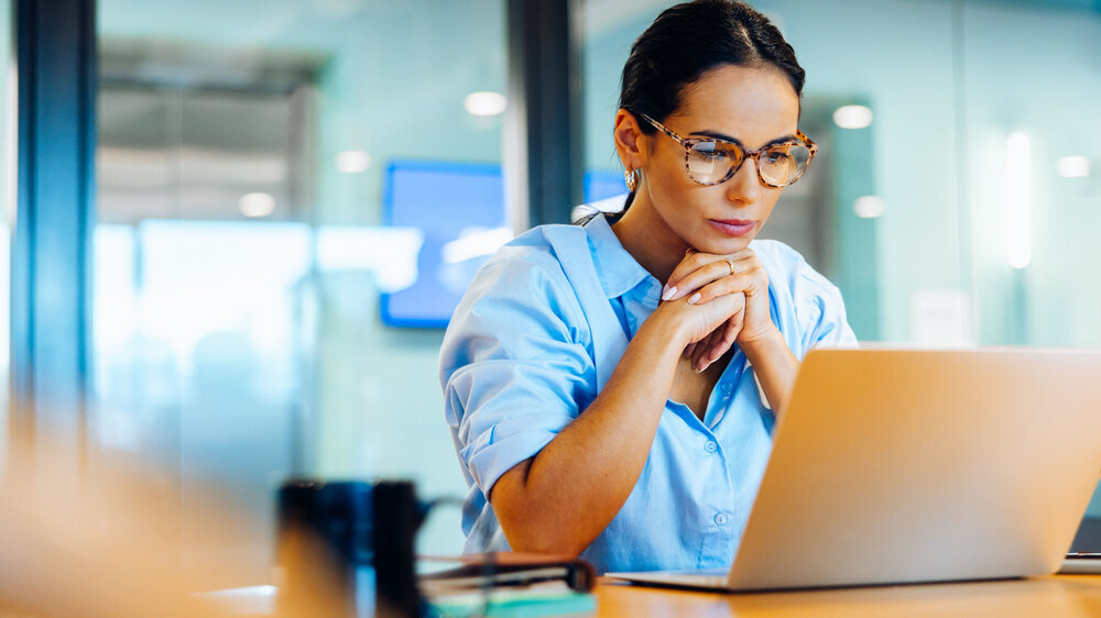 Geschäftsfrau, die in einer professionellen Büroumgebung konzentriert auf ihren Laptop schaut.
