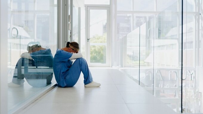 Doctor, stress and woman with depression, burnout and overworked in hospital, deadline and tired. Healthcare, medical professional and nurse crying for mistake, depressed and fatigue with anxiety Symbolfoto Ärztin im Stress ist erschöpft, sitzt auf dem Boden und stützt ihren Kopf auf die Arme.