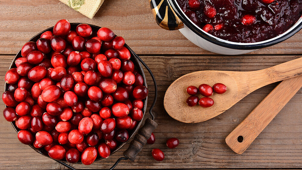 Making Cranberry Sauce for Thanksgiving Overhead of a bucket of cranberries and a pot full of whole cranberry sauce on a rustic wooden table. Cranberry sauce is a traditional Thanksgiving side dish. Horizontal format.