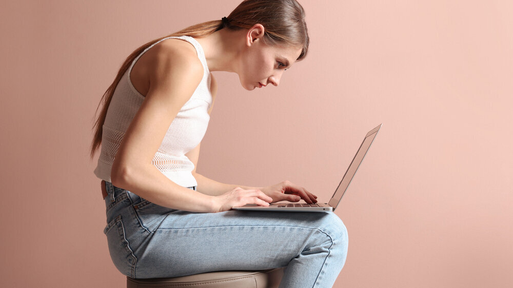 Frau sitzt krumm auf einem Hocker: Schlechte Haltung, sitzen vorm Laptop. Frau sitzt krumm auf einem Hocker: Schlechte Haltung, sitzen vorm Laptop.