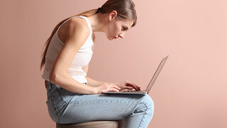 Frau sitzt krumm auf einem Hocker: Schlechte Haltung, sitzen vorm Laptop.
