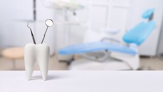 Oral dental hygiene. Healthy white tooth and dentist mirror with explorer probe instrument against blurred dentist Office background with dental chair.