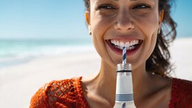 Junge glückliche Frau trinkt Softdrink am Strand