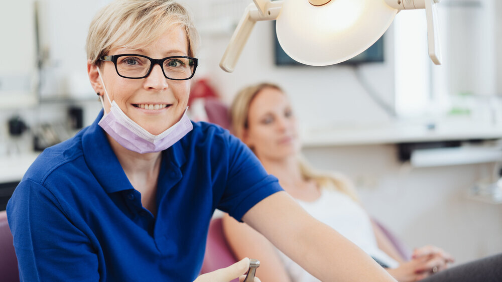 Smiling female dentist wearing mask and glasses Zahnärztin
