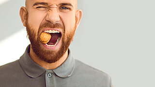 Confident, charismatic, handsome man winks his eye and cracks a hard nut. Close up head shot of a young ginger guy demonstrating his healthy teeth and trying to crack a walnut. Dental health concept