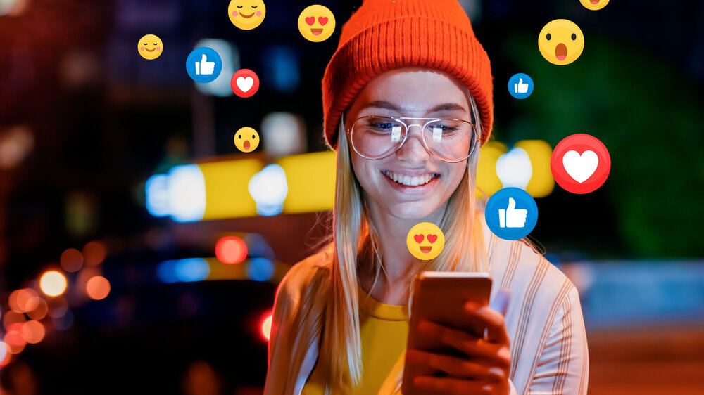 A beautiful young woman blogger, vlogger or influencer is receiving emoji and emoticon reactions in her mobile smart phone device while making a post, sharing or video logging on social media Influencer