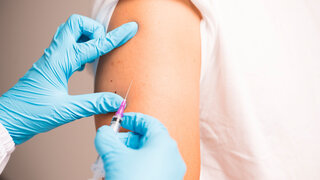 Doctor hand in blue gloves holding influenza vaccine for prevention human.Nurse holding syringe make injection in shoulder of patient in hospital.Covid-19 or coronavirus vaccine.