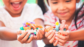 Two asian child girls holding sweet candies in thier hands and share to each other