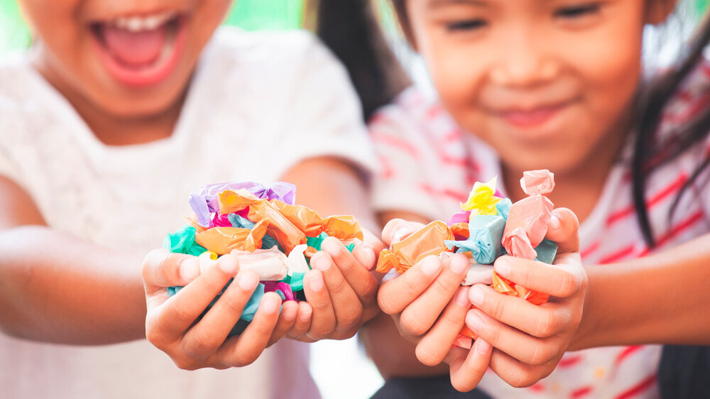 Two asian child girls holding sweet candies in thier hands and share to each other