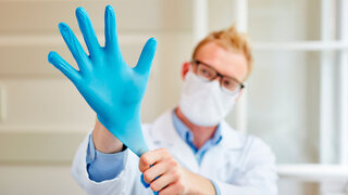 Arzt zieht sich Handschuhe als Arbeitsschutz für die Hygiene an
