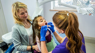 A happy female dentist checks the patient's teeth while her mother supports her in the office of the dental clinic. Dentistry technology technology and healthcare concept