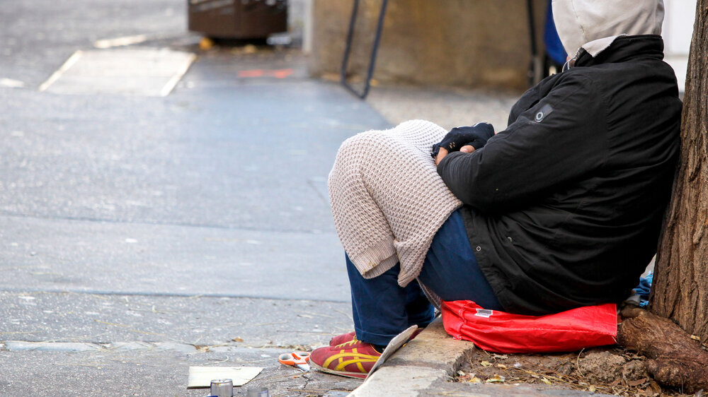 Eine wohnungslose Person sitzt auf dem Bordstein und friert. Eine wohnungslose Person sitzt auf dem Bordstein und friert.