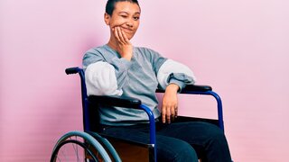 Junge Frau sitzt im Rollstuhl und hält sich die Backe.