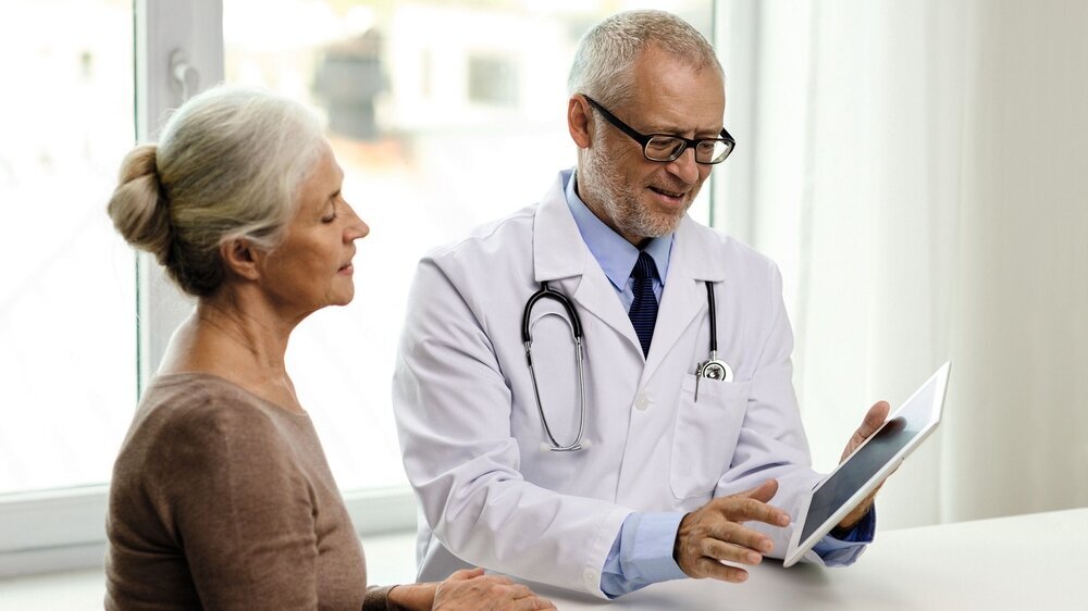 Älterer Art berät Patientin, mit Tablet Älterer Art berät Patientin, mit Tablet