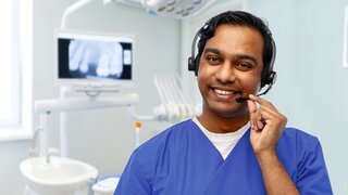 medicine, dentistry and healthcare concept - happy smiling indian doctor or male dentist with headset over dental clinic background