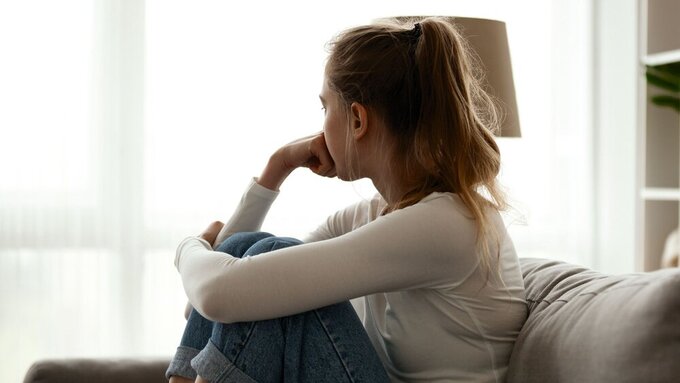 Upset woman sitting on couch alone at home Side view young woman looking away at window sitting on couch at home. Frustrated confused female feels unhappy problem in personal life quarrel break up with boyfriend or unexpected pregnancy concept