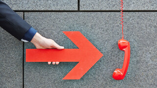 Hand zeigt mit einem roten Pfeil auf ein Telefon an der Wand