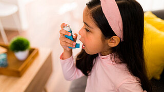 Ein kleines Mädchen verwendet ein Asthma-Spray im Wohnsetting.