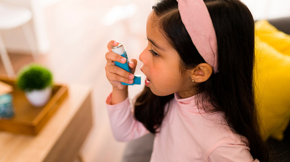 Ein kleines Mädchen verwendet ein Asthma-Spray im Wohnsetting. Ein kleines Mädchen verwendet ein Asthma-Spray im Wohnsetting.