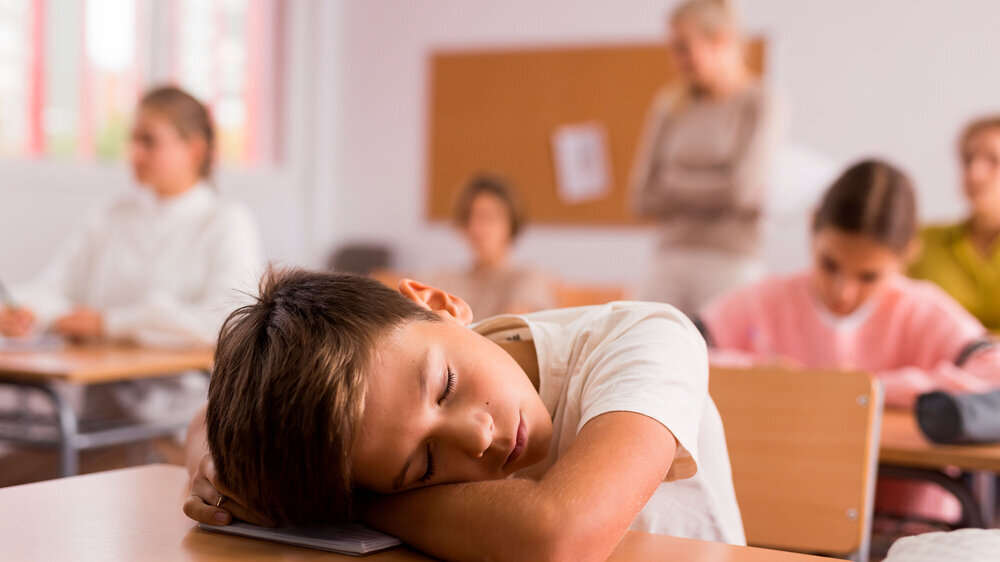 Müder Schüler legt seinen Kopf auf den Arm und schläft in der Schule ein.