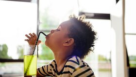 Kleiner Junge trinkt mit Strohhalm aus einem Glas gelber Limo.