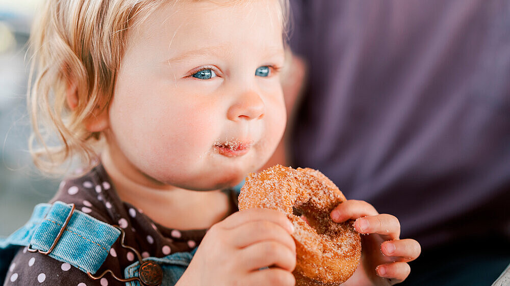 Kleinkind mit gezuckertem Doughnut in der Hand. Kleinkind mit gezuckertem Doughnut in der Hand.