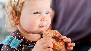 Kleinkind mit gezuckertem Doughnut in der Hand.