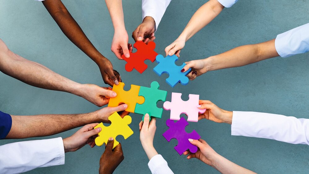 High Angle View Of Medical Team Solving Colorful Jigsaw Puzzle Against Grey Background