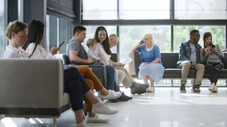 Verschiedene Menschen sitzen im Wartebereich einer Arztpraxis