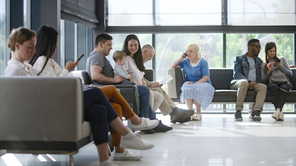Verschiedene Menschen sitzen im Wartebereich einer Arztpraxis