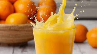 Orangensaft wird in ein Glas mit Spritzer gegossen.