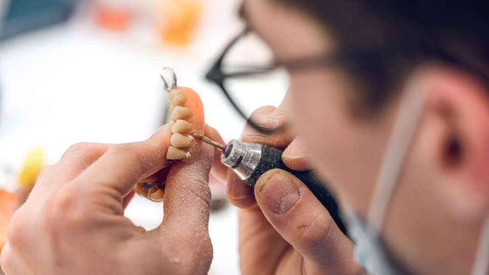 Crop dental technician man grinding denture with rotary machine From above of crop unrecognizable male orthodontist polishing jaw denture while restoring prosthesis in dental laboratory