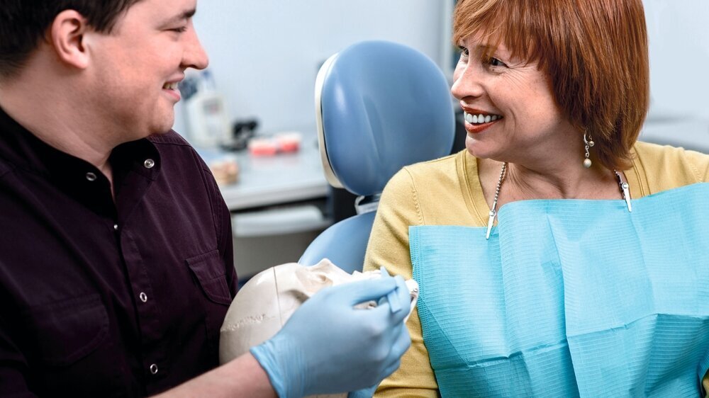 Dentist with patient in the dental office Dentist showing teeth on skull to elder woman patient in the dental office