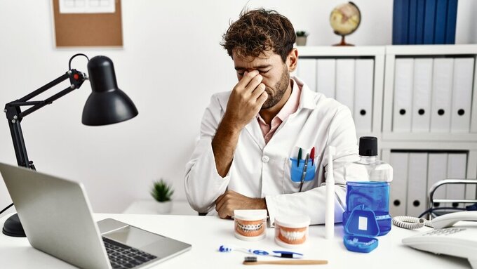 Young hispanic dentist man working at medical clinic tired rubbing nose and eyes feeling fatigue and headache. stress and frustration concept. Young hispanic dentist man working at medical clinic tired rubbing nose and eyes feeling fatigue and headache. stress and frustration concept.