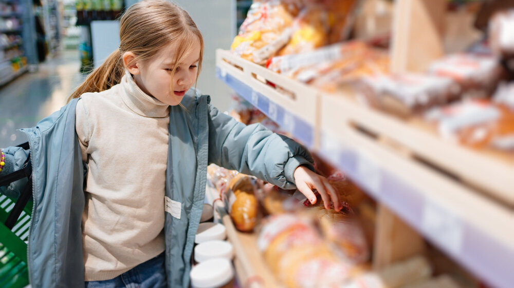 a little girl chooses sweet pastries on the counter in the store. Der „Kindergesundheitsbericht 2022“ der Stiftung Kindergesundheit zeigt einen erheblichen Verbesserungsbedarf bei der Lebensmittel- und Nährstoffzufuhr der Kinder und Jugendlichen. Besonders besorgniserregend sei ein weitaus zu hoher Zuckerverzehr aus Speisen und Getränken.