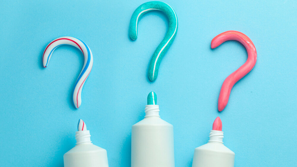 Question mark from toothpaste. Concept of choosing good toothpaste for teeth whitening. Tube of colored toothpaste on blue background. Copy space for text. Question mark from toothpaste. Concept of choosing good toothpaste for teeth whitening. Tube of colored toothpaste on blue background. Copy space for text