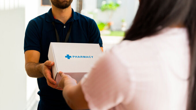 Closeup of a delivery man delivering medication in a white box with the word pharmacy on it to a woman Versandapotheke