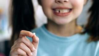 Kleines Mädchen hält verlorenen Milchzahn zwischen den Fingern.