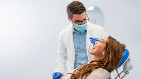 Zahnarzt bei der Besprechung mit einer Patientin, die auf dem Behandlungsstuhl sitzt.