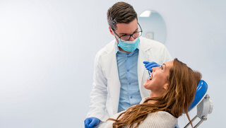 Zahnarzt bei der Besprechung mit einer Patientin, die auf dem Behandlungsstuhl sitzt.