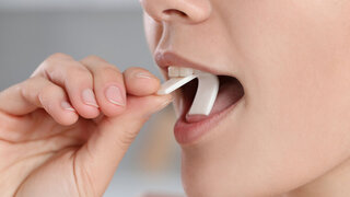Woman putting chewing gum into mouth on blurred background, closeup