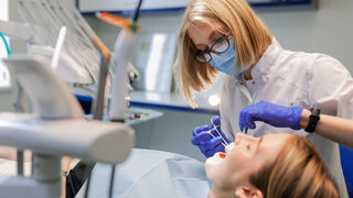 Zahnärztin mit Mundschutz arbeitet über einen Patienten gebeugt.